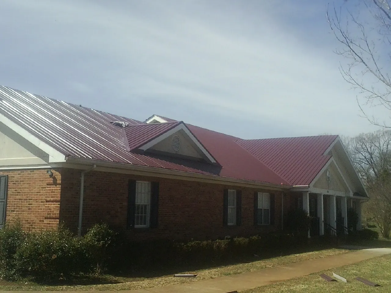 Red metal roof with gabled entries on a long brick building, from a Hail Damage Roof Repair job in Duluth
